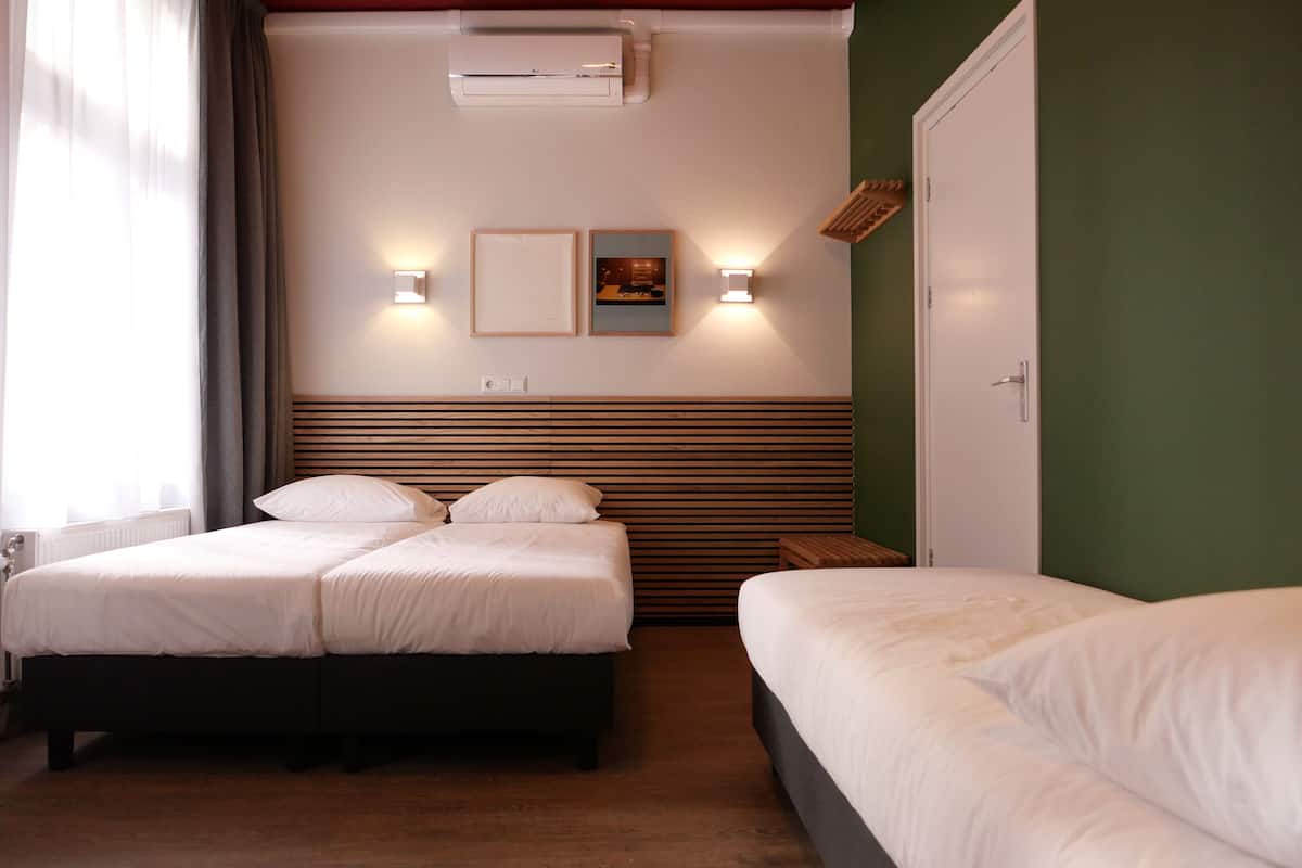 A hotel room with two beds, a wooden headboard, a wall-mounted air conditioner, and two wall-mounted lights.