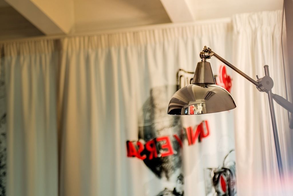 A room with a ceiling fan, a window with white curtains, and a wall with a partial view of a poster.