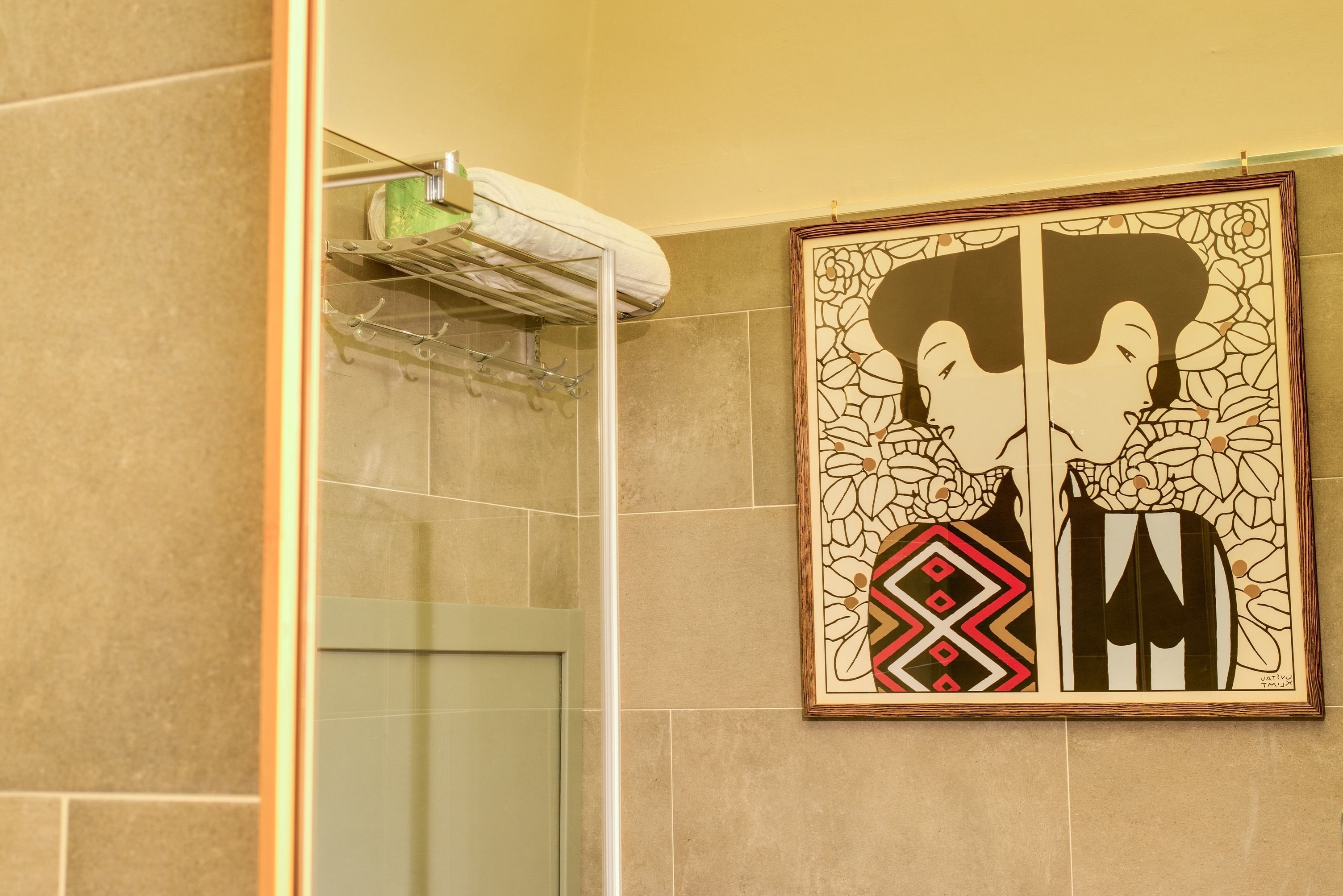 A bathroom with a glass shower enclosure, a towel rack with a white towel, and a framed artwork on the wall.