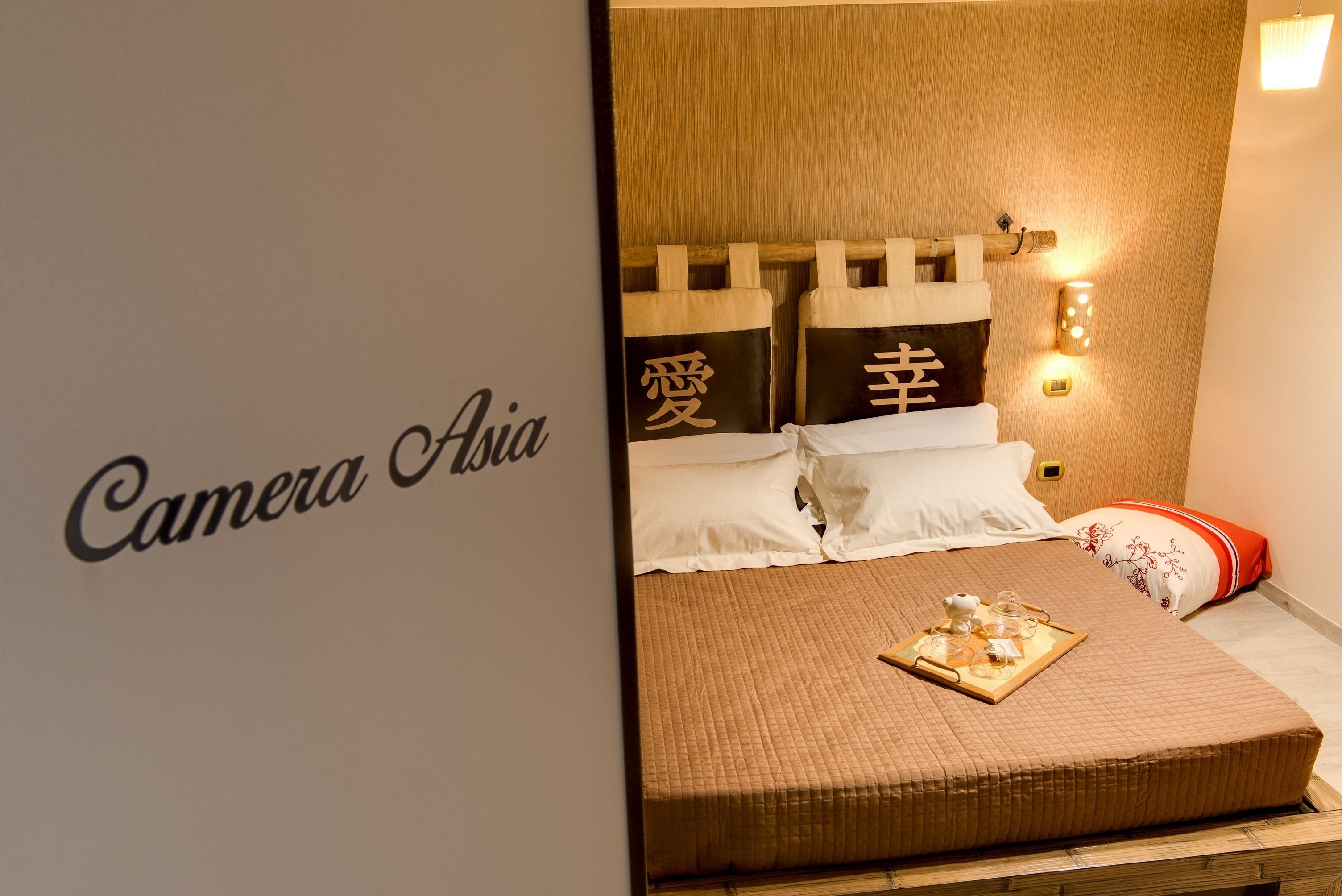 A neatly made bed with a brown quilt, pillows with Chinese characters, and a tray with tea and snacks.