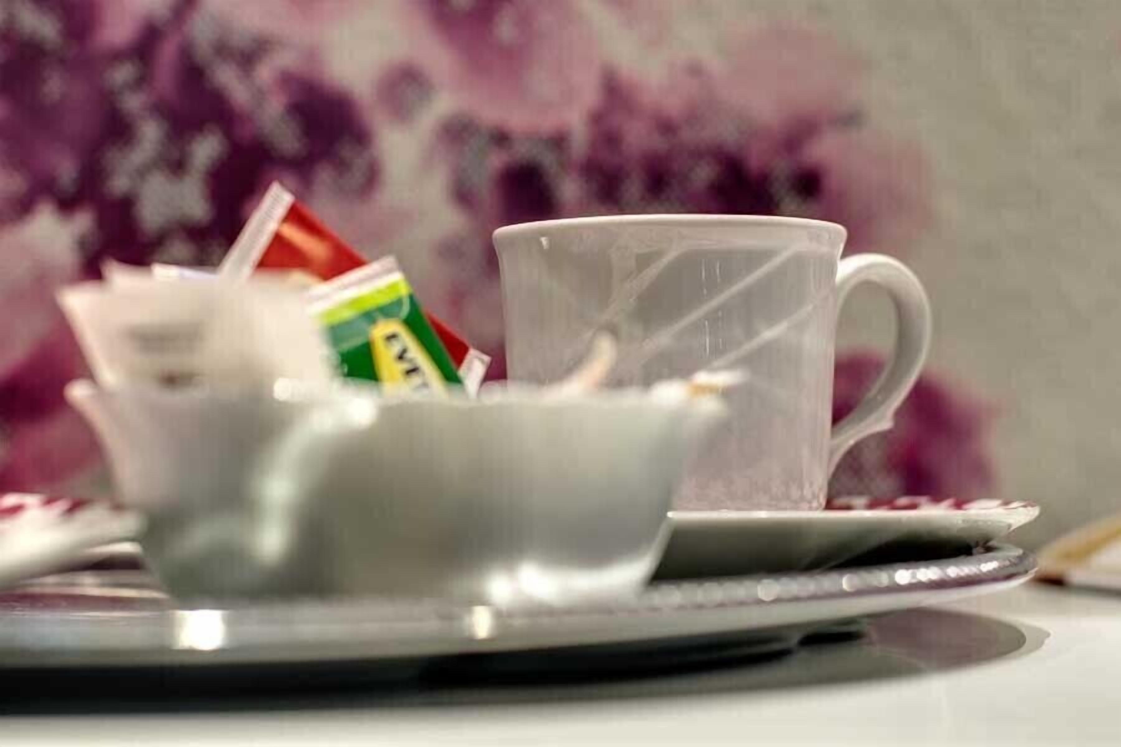 Eine weiße Tasse und ein Untertasse auf einem Tablett vor einem unscharfen Blumenhintergrund.