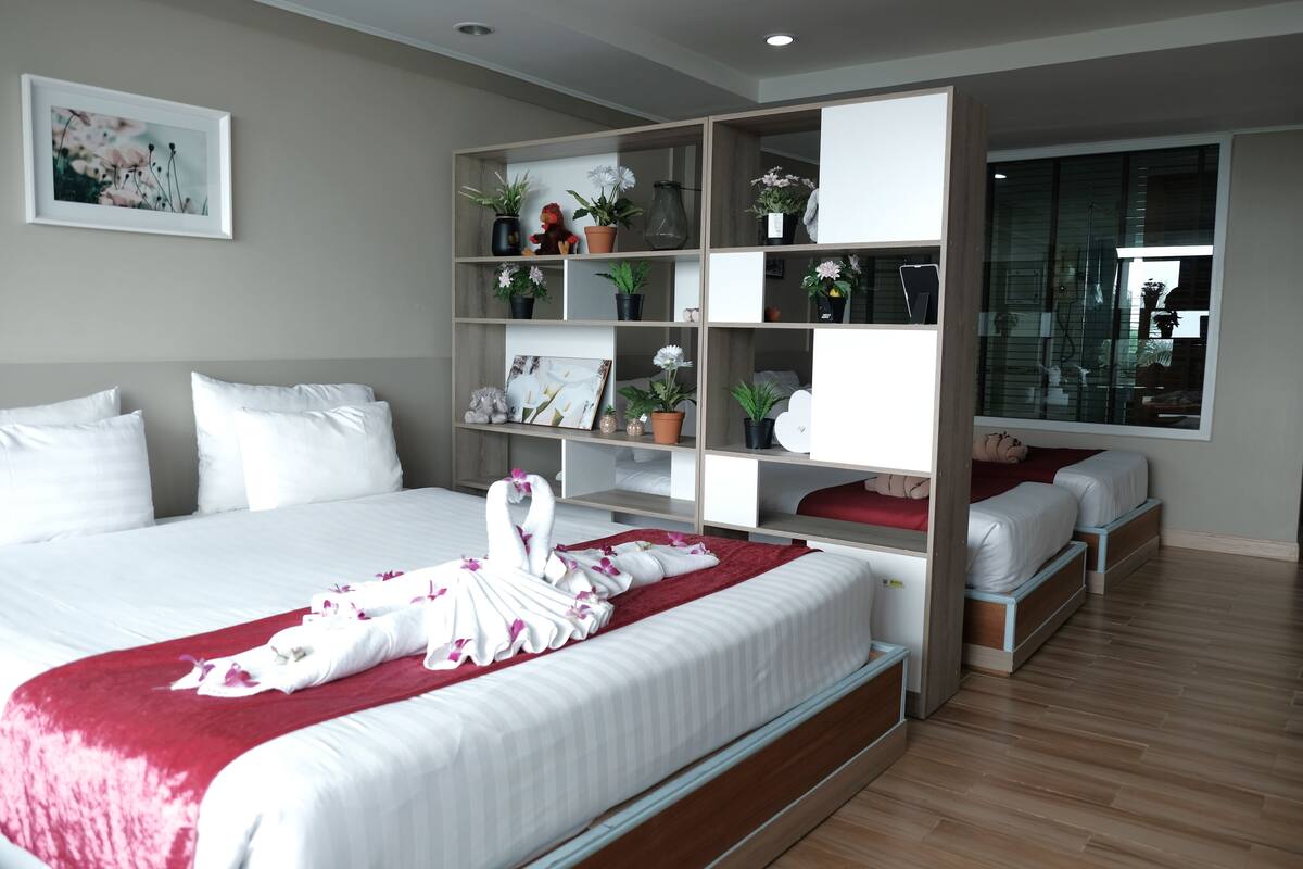 A modern hotel room with a large bed, a built-in wardrobe, a bedside table, and a large window.