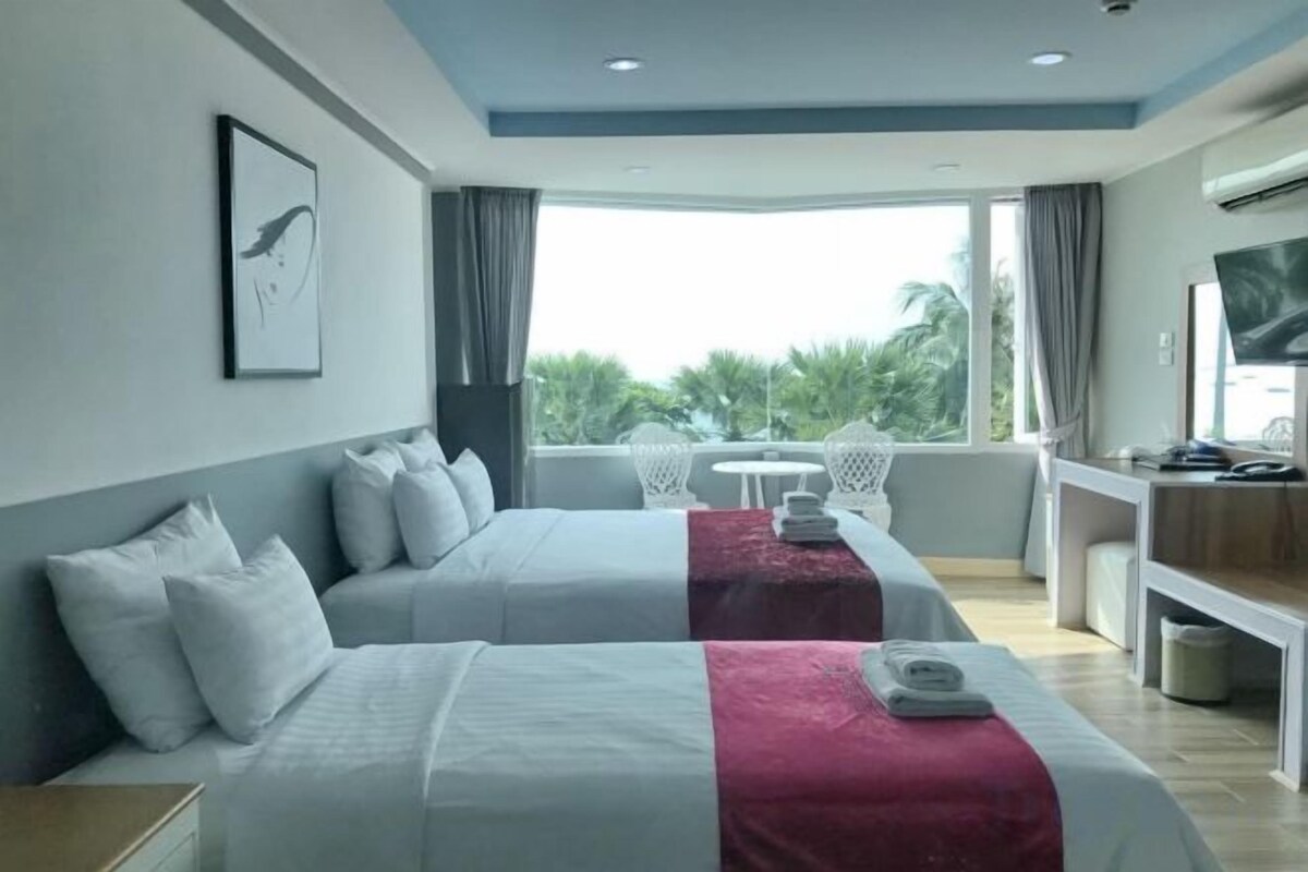 Ein Hotelzimmer mit zwei Betten, einem Schreibtisch, einem Fernseher und einem Balkon mit Blick ins Freie.