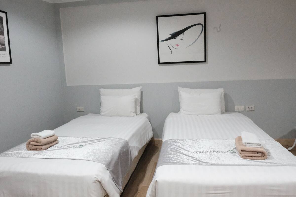 A hotel room with two single beds, white bedding, and a framed artwork on the wall.