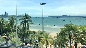 Una playa con palmeras, un horizonte urbano al fondo y barcos en el agua.