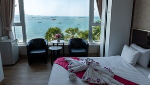 Habitación de hotel con cama, dos sillas, una mesita y vistas al mar.