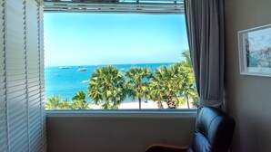 Una habitación con un ventanal grande que da a una playa, palmeras y el océano.