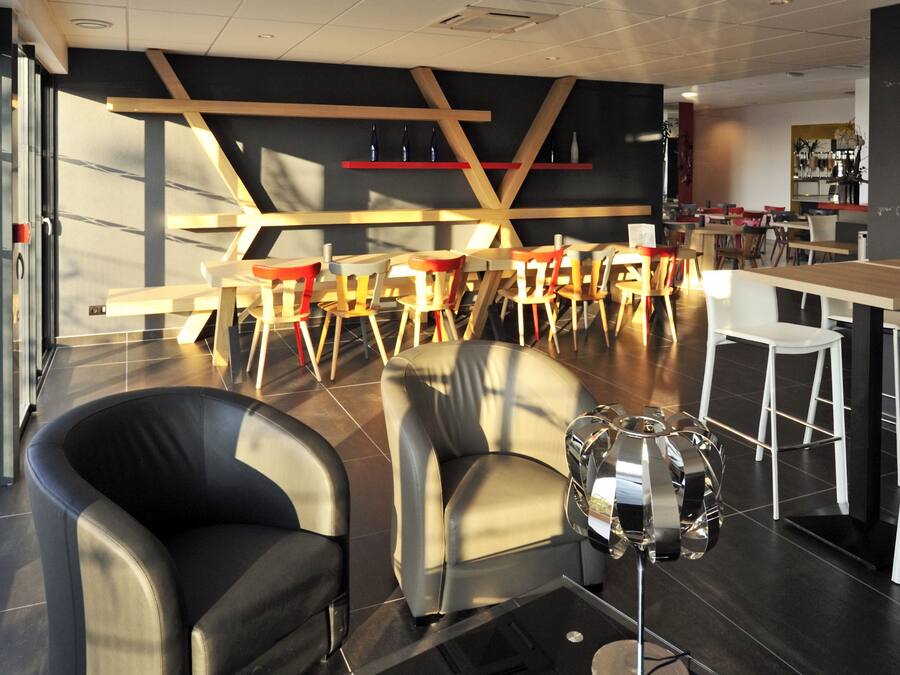 Un interior moderno con una zona de estar que incluye dos sillones de cuero negro, una mesa de centro de vidrio y una pieza decorativa original. La habitación presenta un diseño contemporáneo con detalles de madera y una barra en el fondo.