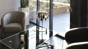 A modern room with a glass table, leather chairs, a potted plant, and a view of the city through large windows.