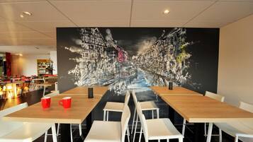 A modern dining area with a large mural of a cityscape on the wall, white chairs, and wooden tables.