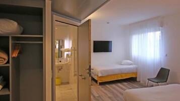 Una habitación de hotel con piso de madera, una cama, una silla, un televisor y un armario.