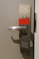 Una puerta con picaporte metálico y panel rojo, con un aviso multilingüe que indica no molestar.