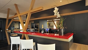 A modern bar area with a red countertop, white chairs, and wooden beams.