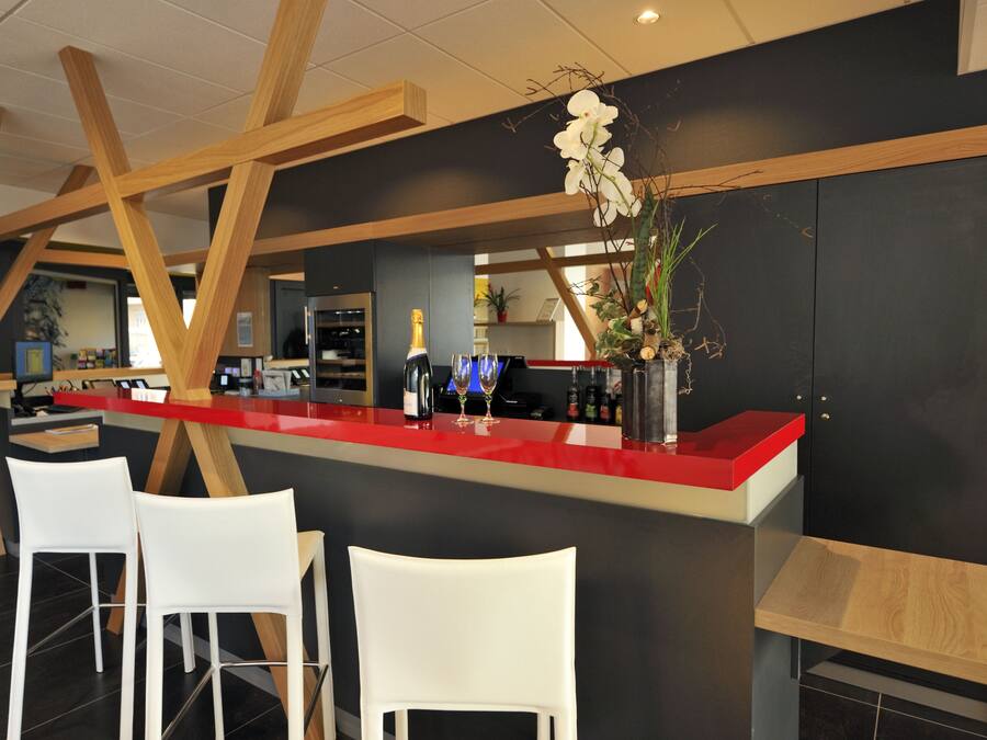 A modern bar area with a red countertop, white chairs, and wooden beams.