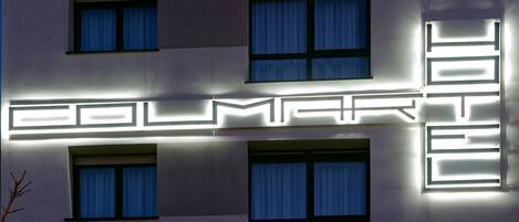 A building facade with illuminated geometric patterns and multiple windows with curtains.