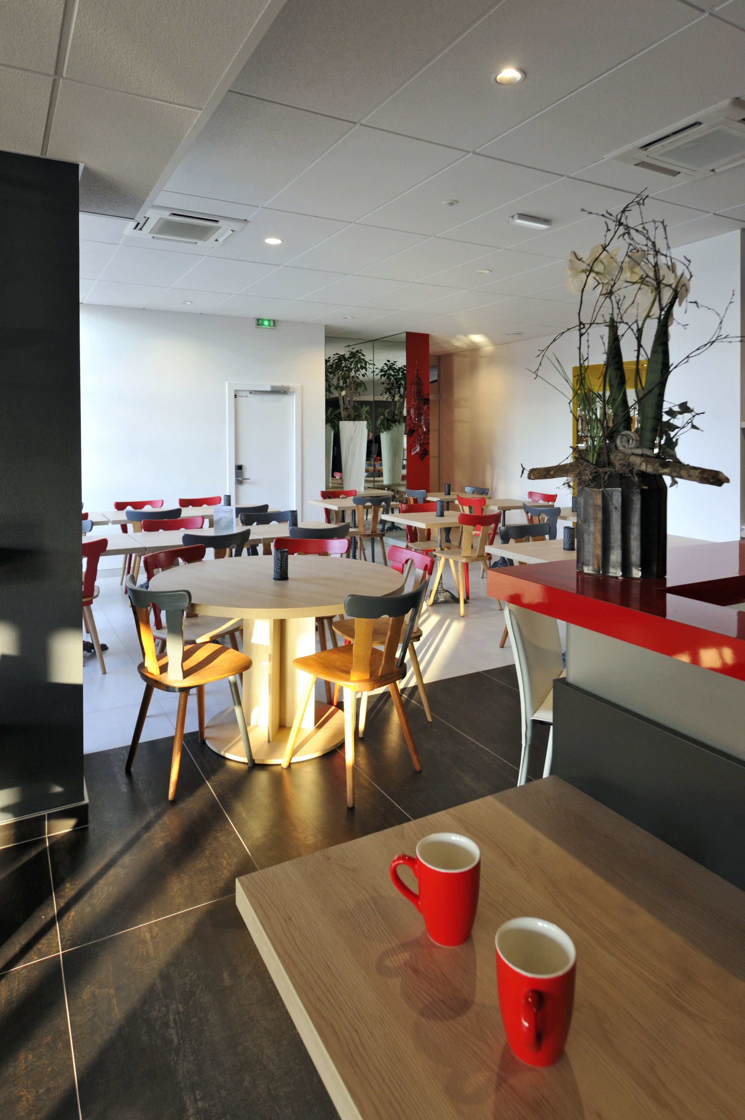 A modern dining area with round tables and chairs, a red counter, and a potted plant.
