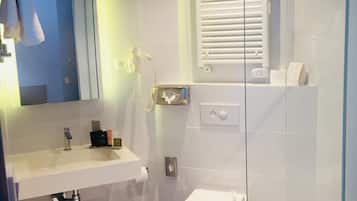Un baño moderno con cabina de ducha de vidrio, inodoro blanco, lavabo con espejo y un perchero para toallas.
