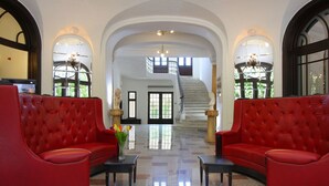 A spacious lobby with red upholstered seating, a polished floor, and a grand staircase leading to upper levels. - Hotel Palace (Prajila)