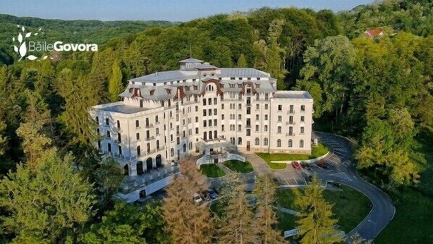 A large, multi-story building surrounded by dense greenery, with a curved driveway leading to a parking area. - Hotel Palace (Prajila)