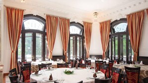 A formal dining room with round tables, red and gold curtains, and large windows. - Hotel Palace (Prajila)
