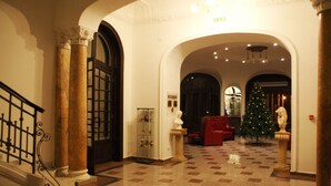 A grand hallway with marble columns, a red sofa, and a Christmas tree. - Hotel Palace (Prajila)