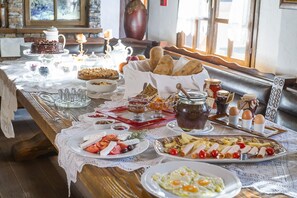 A breakfast table with various dishes, including eggs, bread, and pastries, set in a cozy room with a wooden bench and a vase.