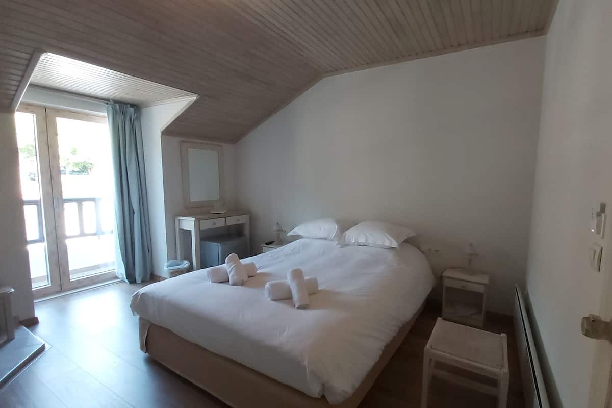 A bedroom with a large bed, a bedside table, a nightstand, a small stool, and a window with curtains.
