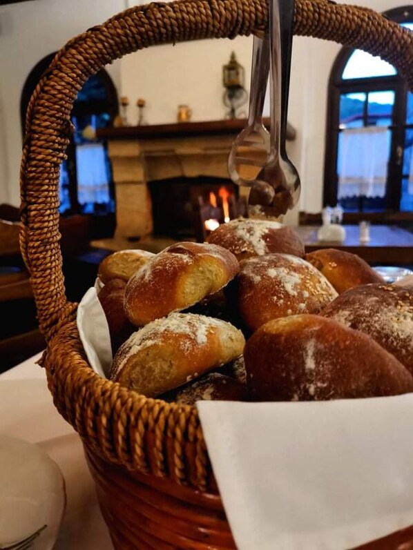 A basket of freshly baked bread on a table in a room with a fireplace and arched windows.