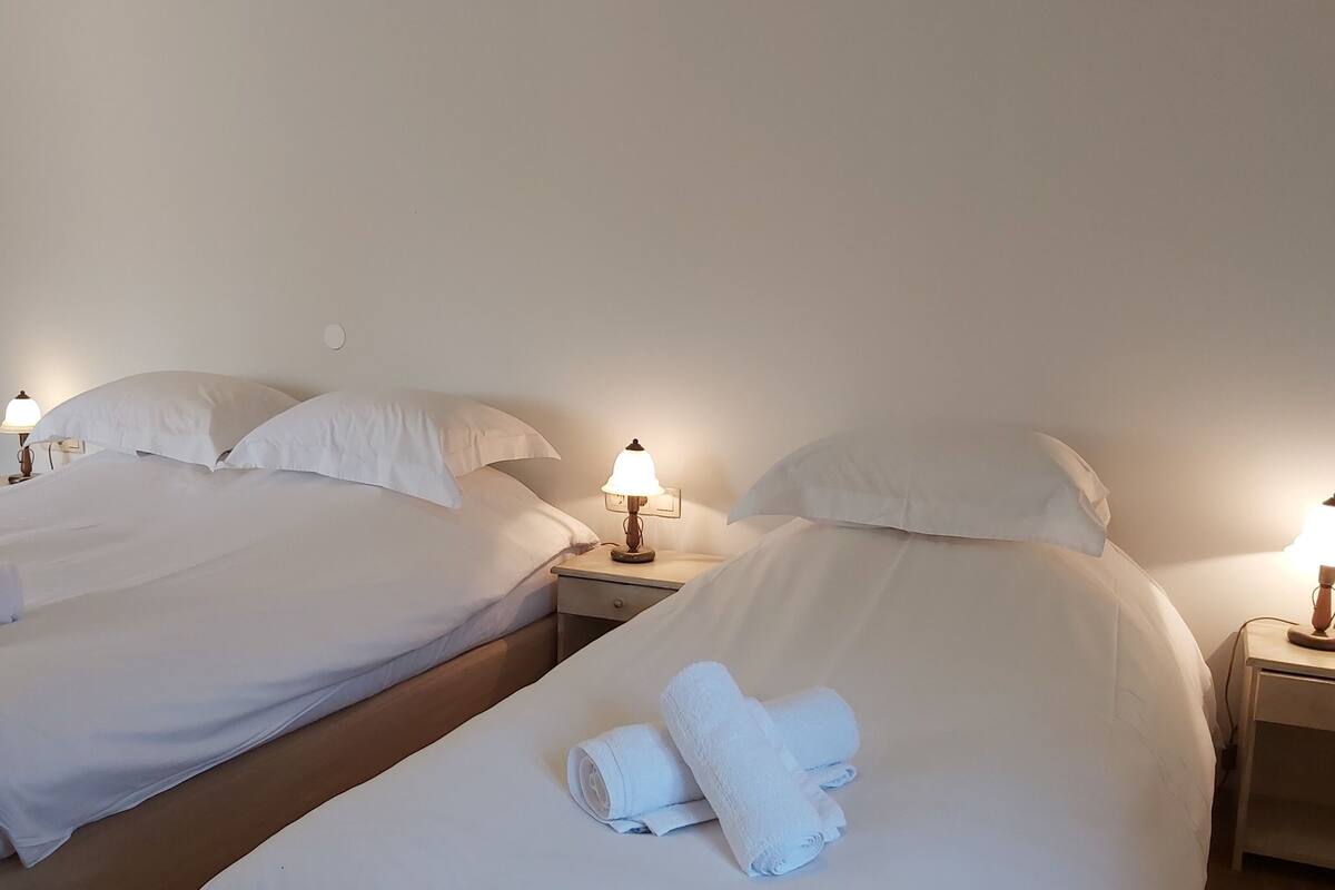 A hotel room with two beds, each with white linens and pillows, and bedside lamps.