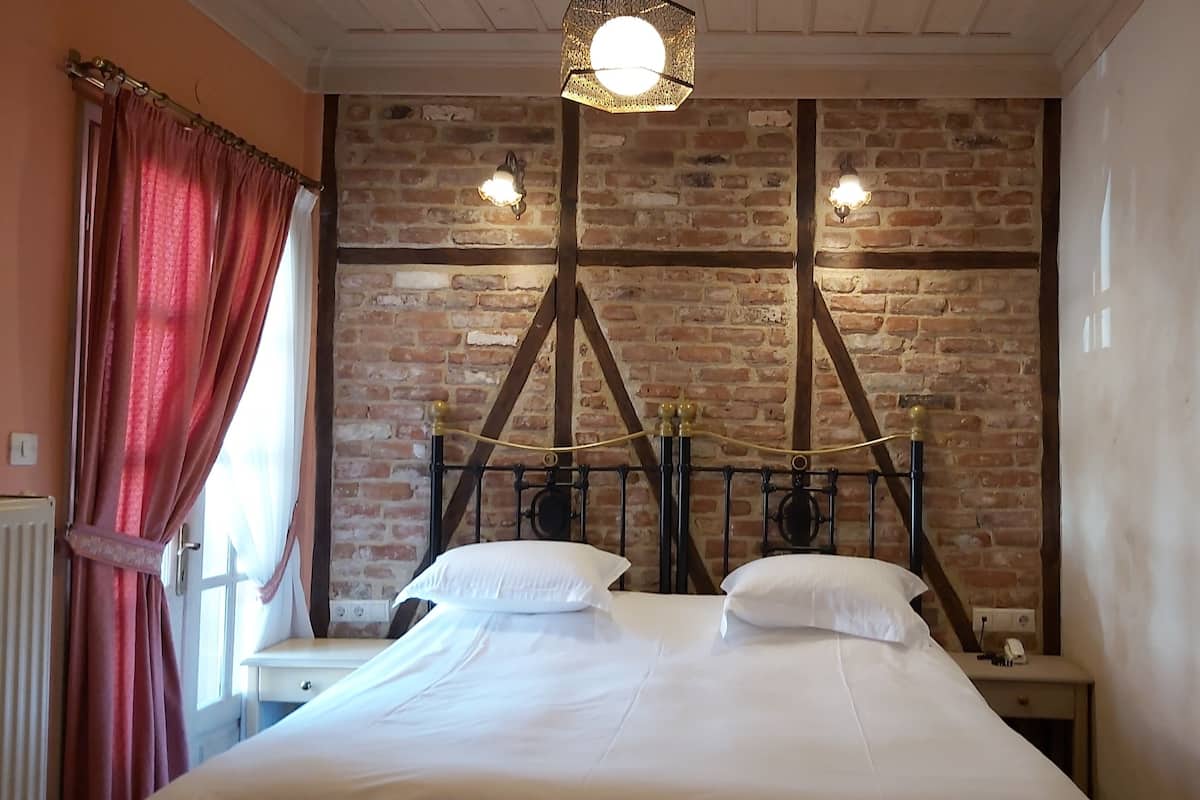 A bedroom with a brick wall, a bed with white bedding, two bedside tables, and a hanging light fixture.