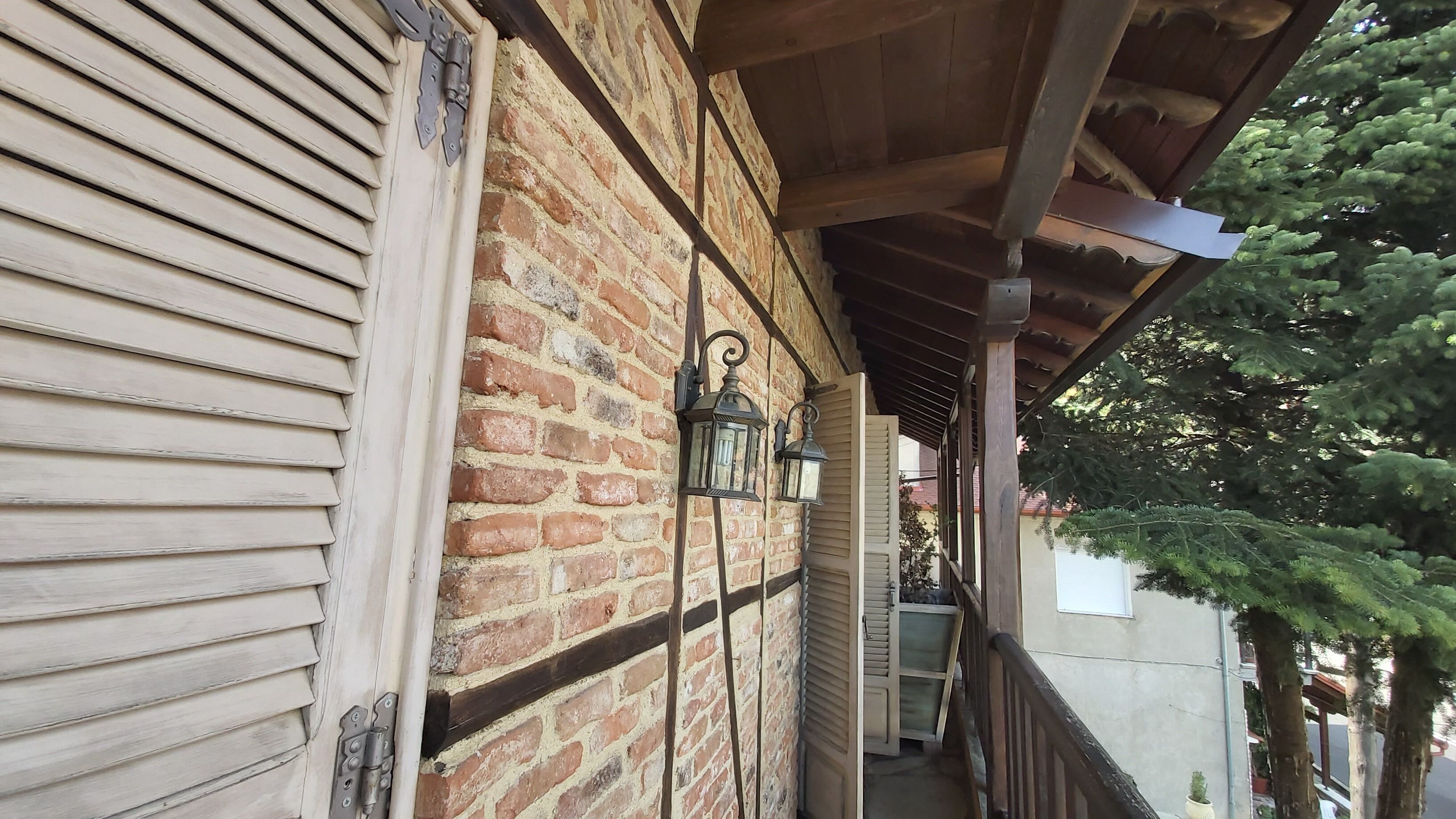 A covered porch with a brick wall, wooden shutters, and two lantern-style lights.