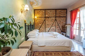 A room with a large bed, a brick wall, a radiator, and a window with curtains.