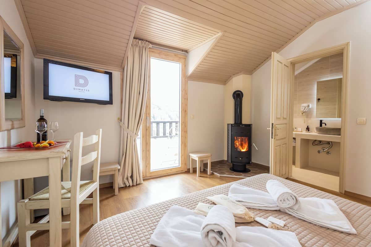 A hotel room with a bed, a TV, a fireplace, a small table, and a chair.