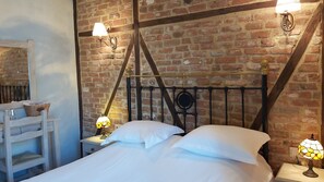 A bedroom with a brick wall, a metal bed frame, white bedding, and two table lamps.