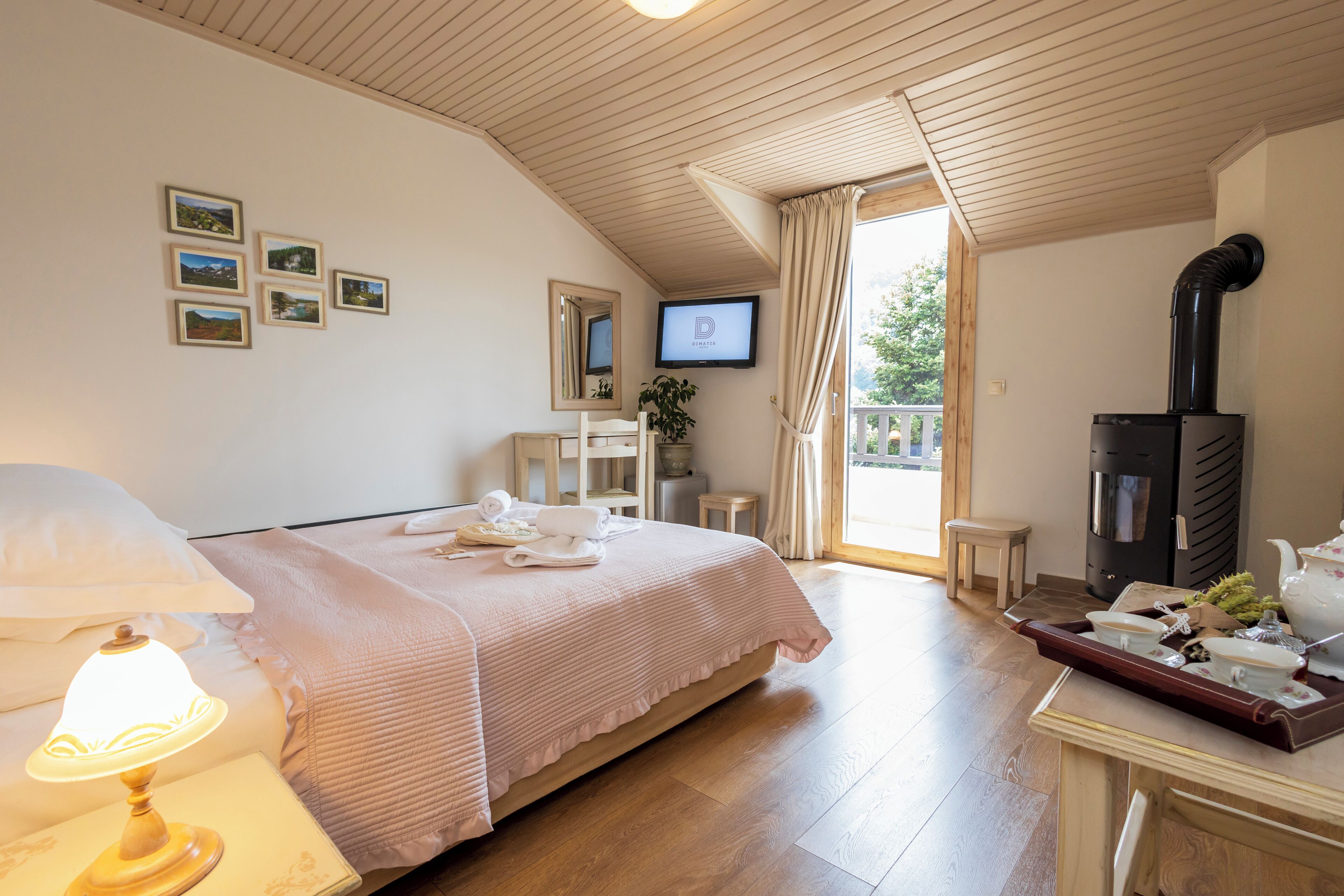 Una habitación de hotel con cama, televisión, chimenea, escritorio con bandeja de té y utensilios, y ventana con cortinas.