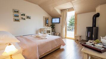 Una habitación de hotel con cama, televisión, chimenea, escritorio con bandeja de té y utensilios, y ventana con cortinas.