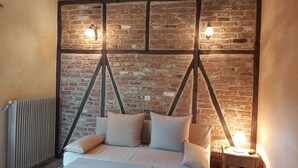 Une chambre avec un mur en briques, un lit avec des oreillers, un radiateur et deux lampes fixées au mur.