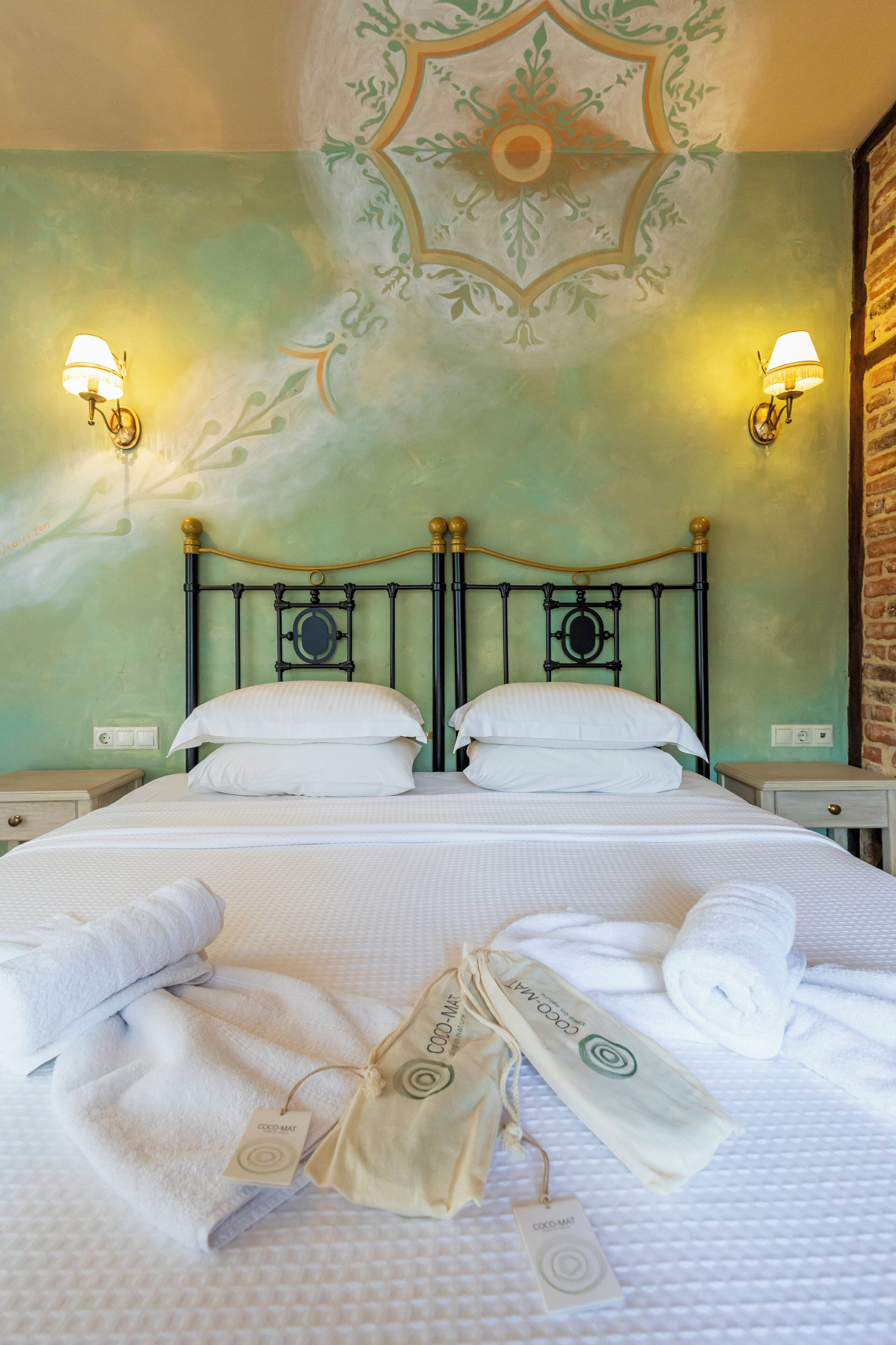 A neatly made bed with white linens and towels, a decorative ceiling mural, and wall-mounted lamps.