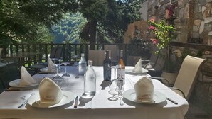 Un espace de restauration en plein air avec une table dressée pour deux personnes, agrémentée de serviettes blanches, de verres à vin et d’une bouteille de vin.