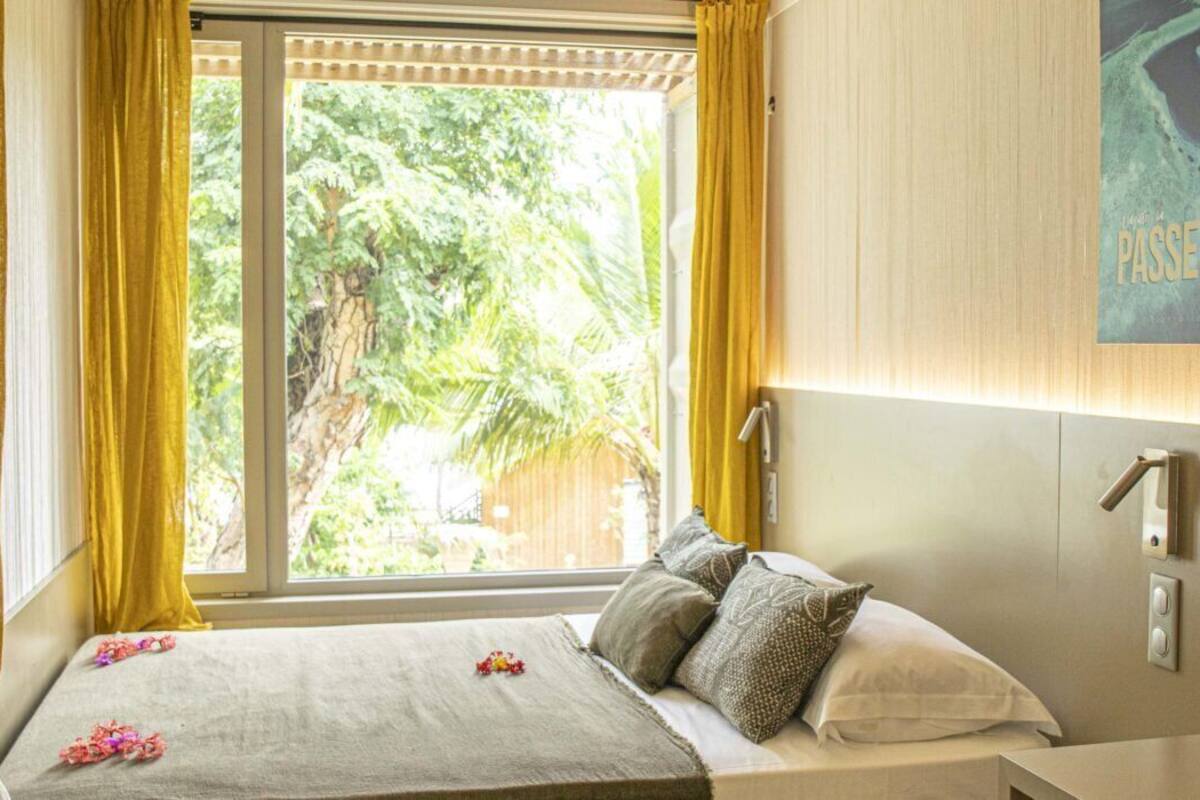 A bedroom with a bed, curtains, a window, a wall-mounted light, and a painting.