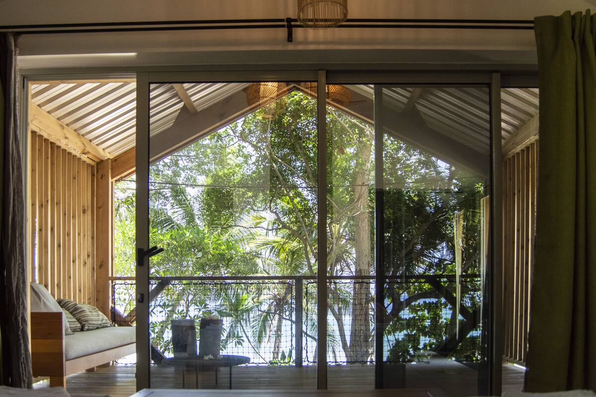 A room with a large sliding glass door leading to a balcony with a view of lush greenery.