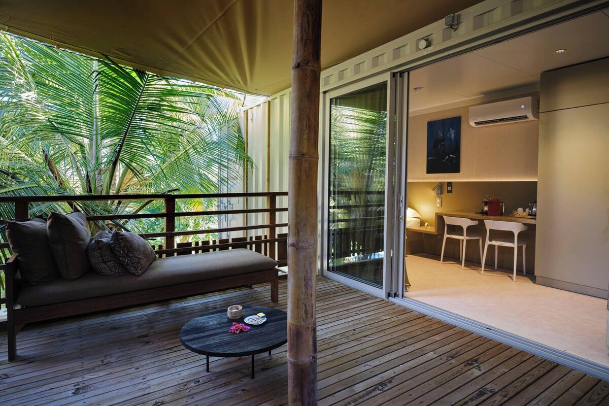 A wooden deck with a sofa and a small table, a sliding glass door leading to a kitchen area with a dining table and chairs.