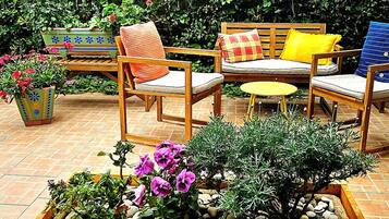 A wooden planter box with flowers and pebbles, surrounded by outdoor furniture including chairs and a table.