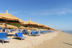 Una playa con filas de sillas azules y sombrillas de paja.