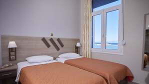 A hotel room with two beds, a nightstand, a lamp, a window with a view, and a mirror. - Amalia Rooms (Chios)
