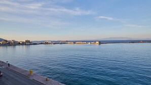 A waterfront view with a paved walkway, a road, and buildings in the distance. - Amalia Rooms (Chios)