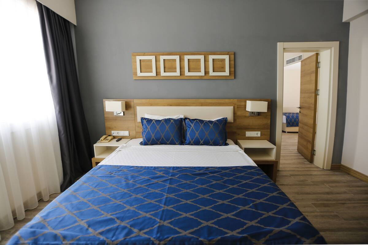 Une chambre d’hôtel avec un grand lit, une tête de lit en bois, deux tables de chevet avec des lampes et un miroir au mur.