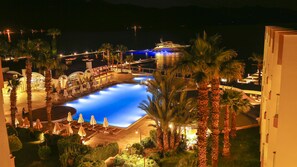 A nighttime view of a resort with a large swimming pool, palm trees, and a yacht docked nearby. - Fortezza Beach Resort (Marmaris)