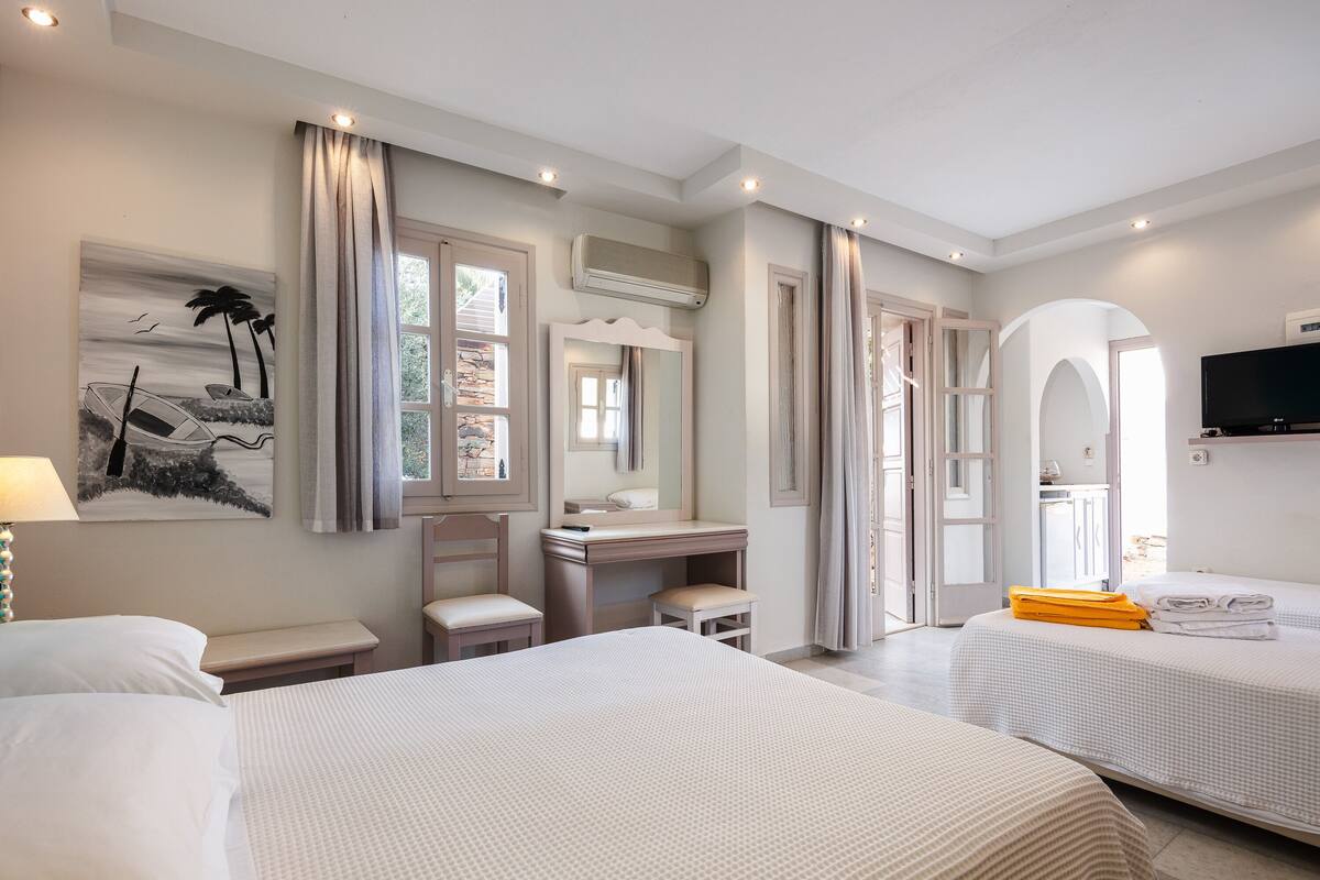 A hotel room with two beds, a desk, a chair, a vanity with a mirror, and a television.