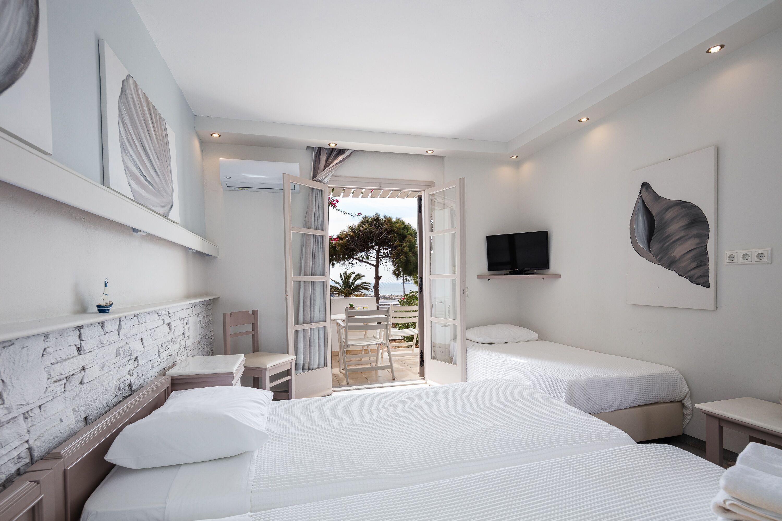 Habitación de hotel moderna con dos camas, televisión y balcón con vista al mar.